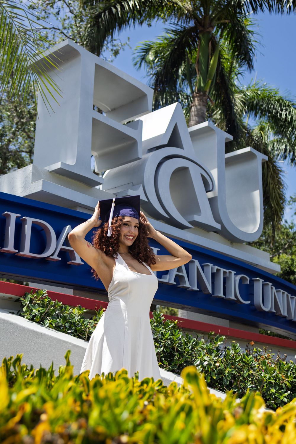 Florida Atlantic University entrance sign with palm trees and yellow flowers in the foreground.