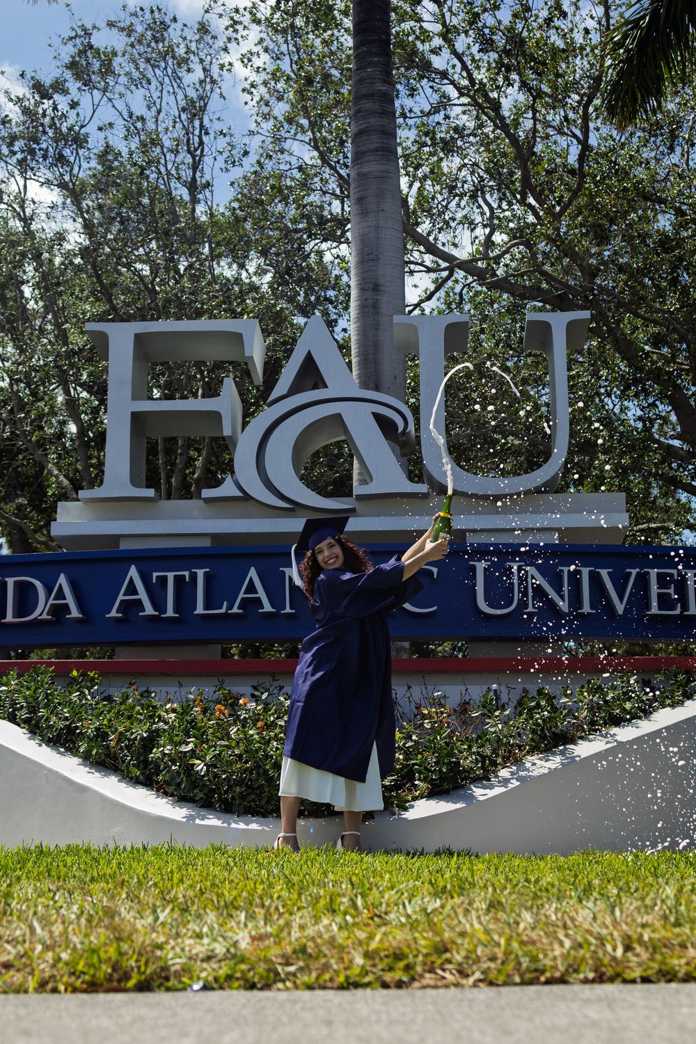 Graduate posing in front of Florida Atlantic University entrance sign.