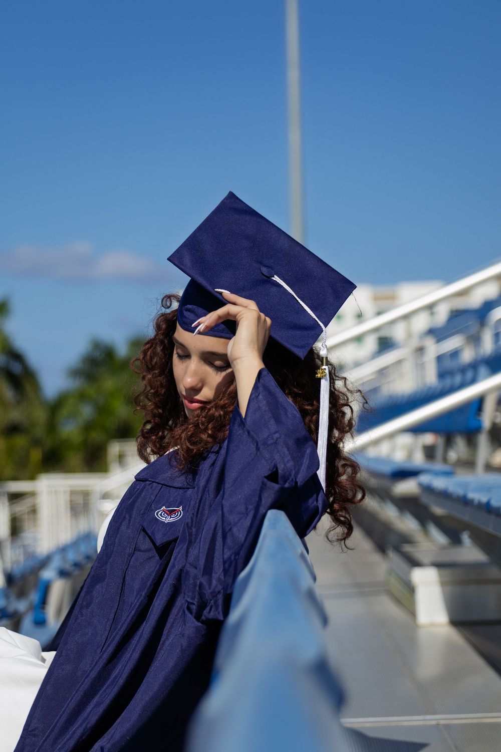 Graduate in navy blue cap and gown against bright blue sky background.