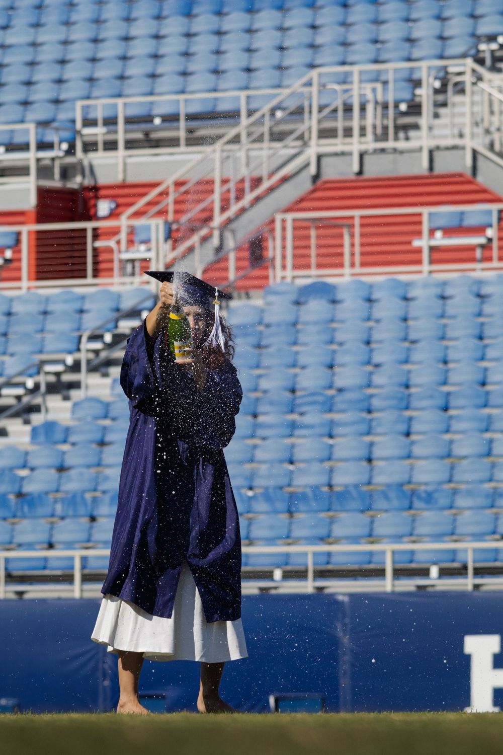 Graduate celebrating in empty stadium with blue seats in background.