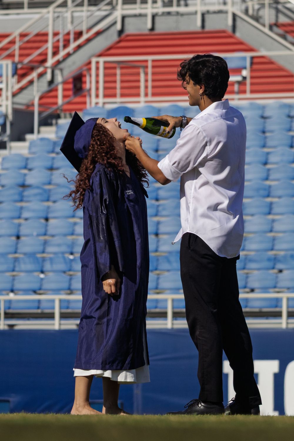 Students in graduation gowns and caps celebrate during a commencement ceremony at a stadium.
