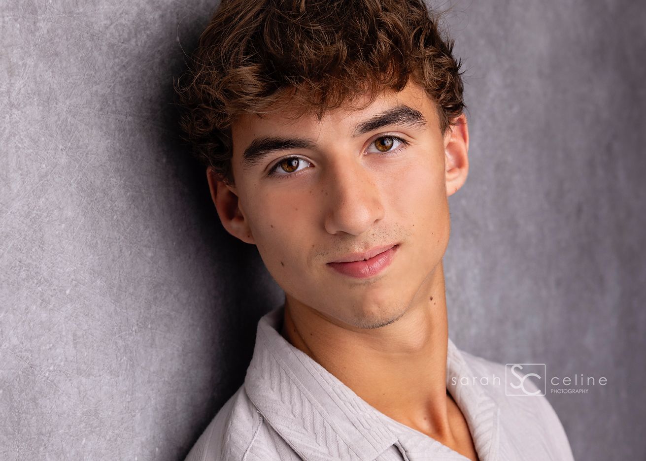 Professional headshot portrait of someone in a white button-up shirt against a textured gray background.