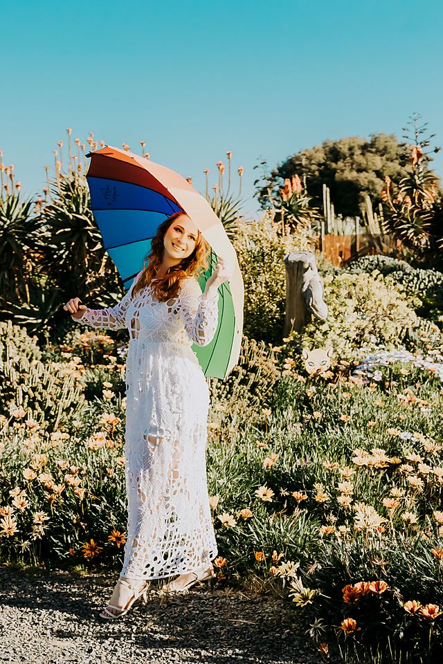 Vintage-style white lace dress paired with colorful parasol in garden setting with blooming flowers.