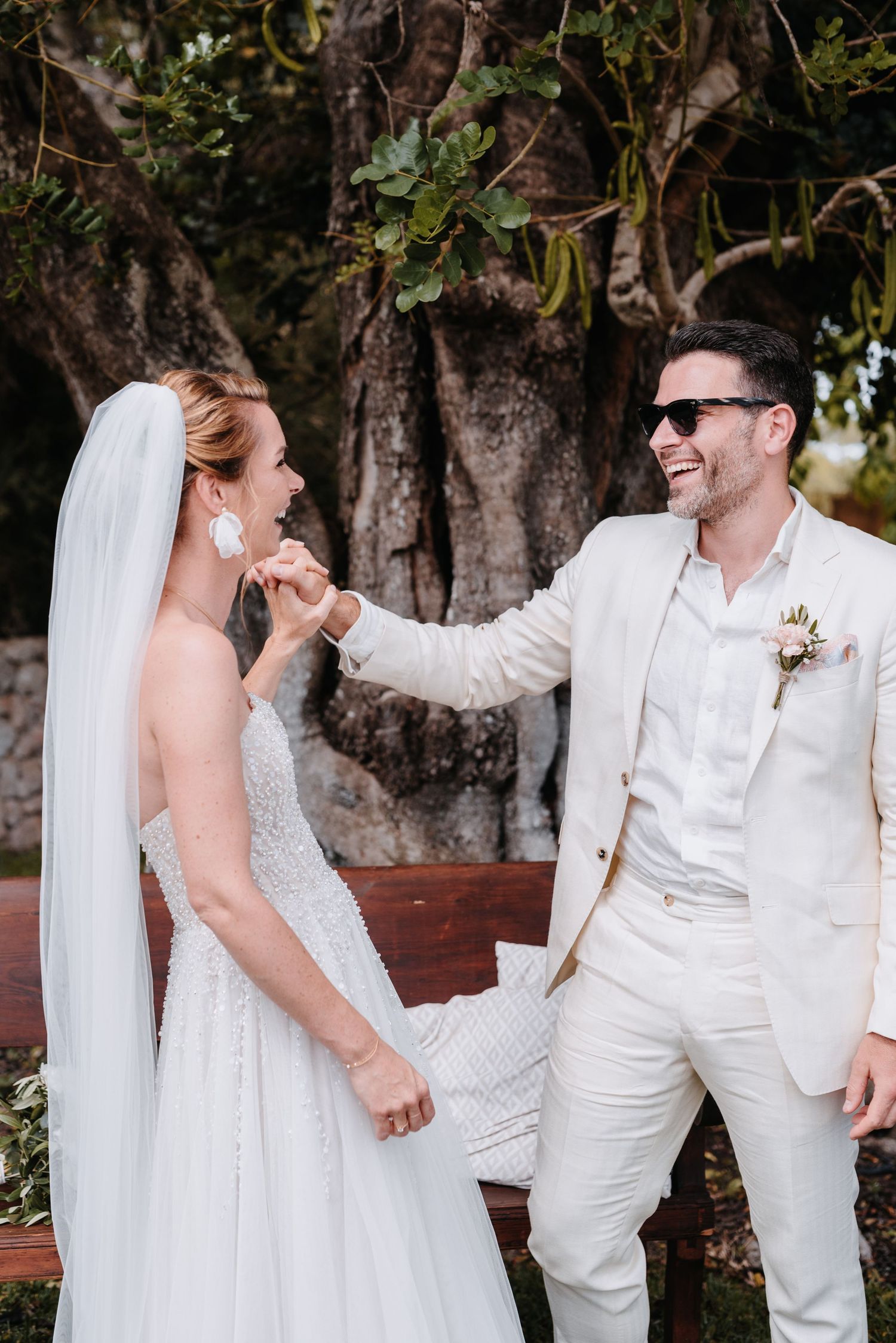 Ein Hochzeitspaar teilt freudige, ungezwungene Momente während der Trauung im Freien mit Bäumen im Hintergrund auf der Finca auf Mallorca.