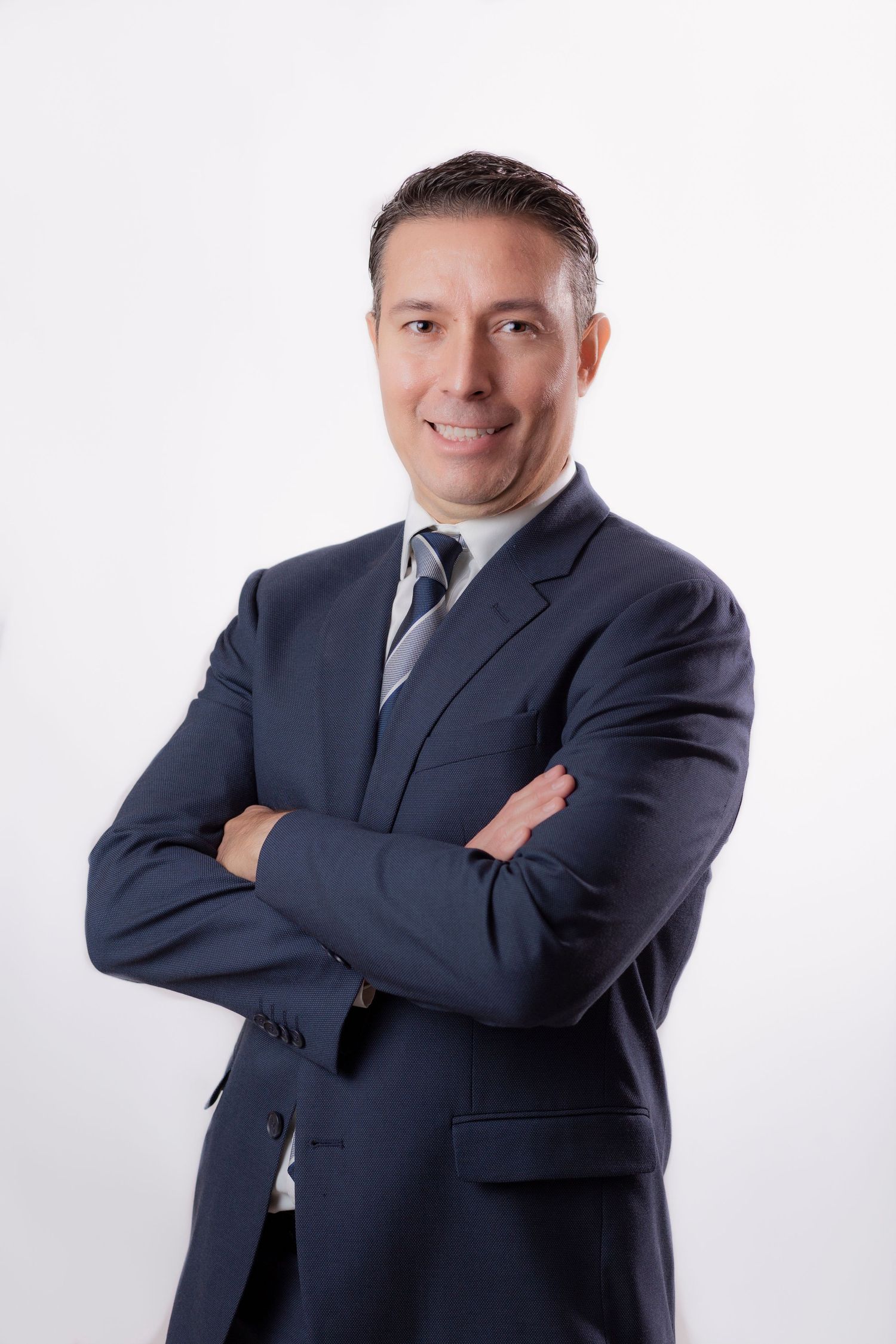 Professional portrait of person in navy suit with crossed arms against white background.