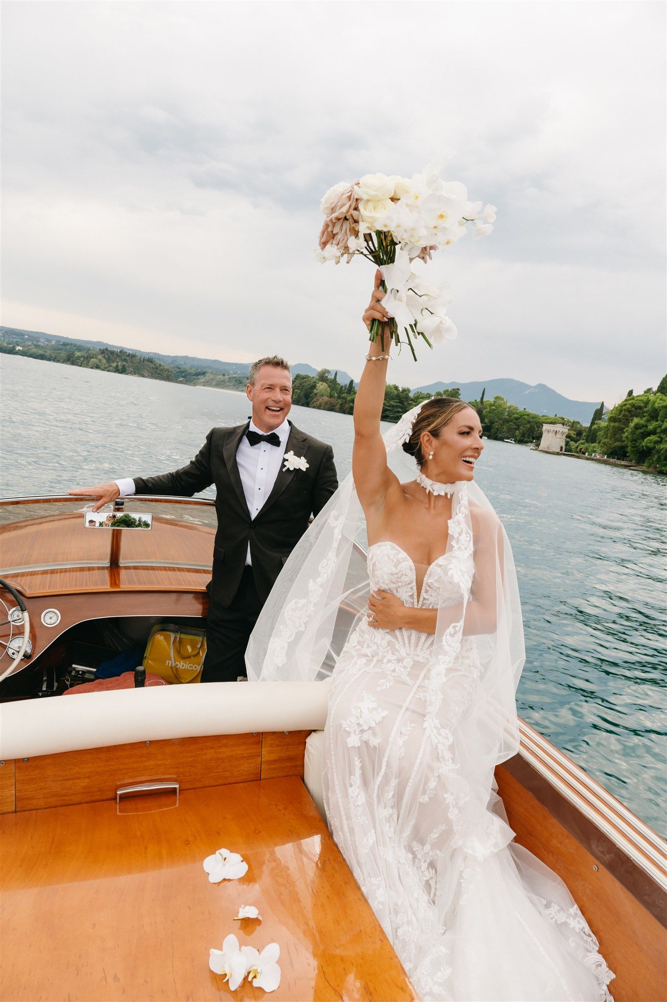 Joyful wedding celebration aboard a classic wooden boat on a scenic lake.