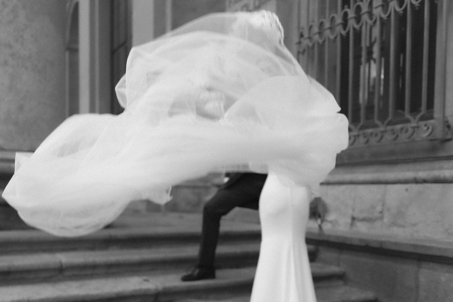 A long, flowy white wedding dress and veil twirl elegantly in an ornate stone building setting.