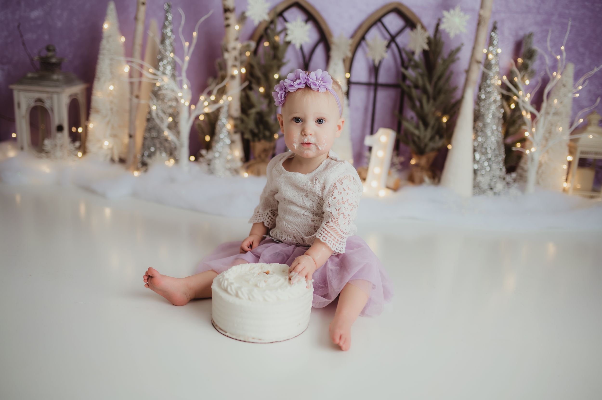 Children enjoy cake smash photo session with winter wonderland decorations and silver stars in background.