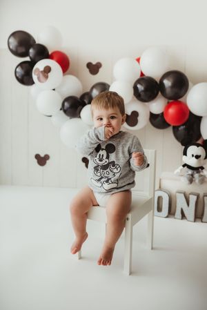 Mickey Mouse themed baby photo with black, white and red balloons against a white wall and matching decor.