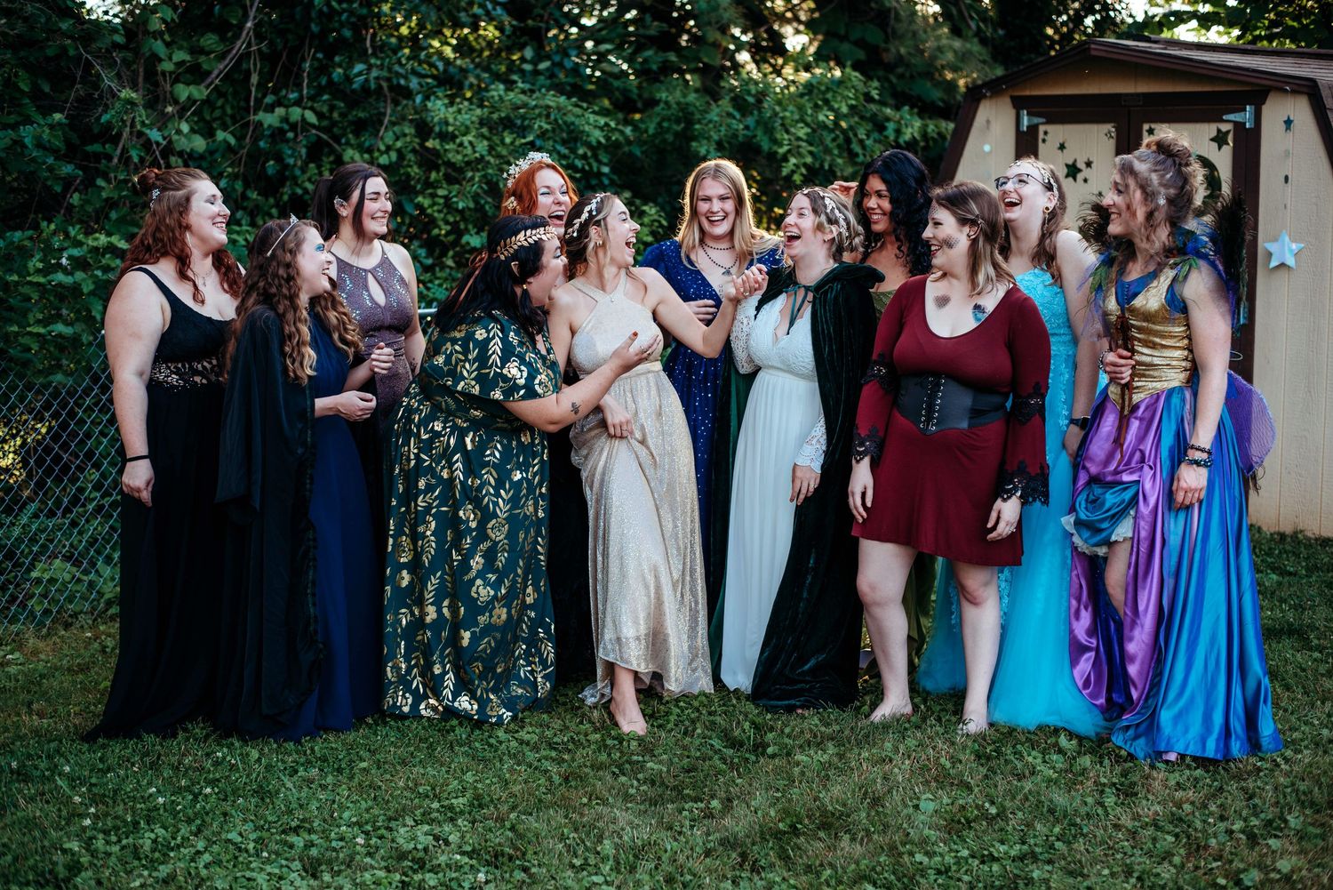 Group of women dressed as fairies at the Starfall Ball, wearing flowing gowns with shimmering wings, standing together in a woodland setting