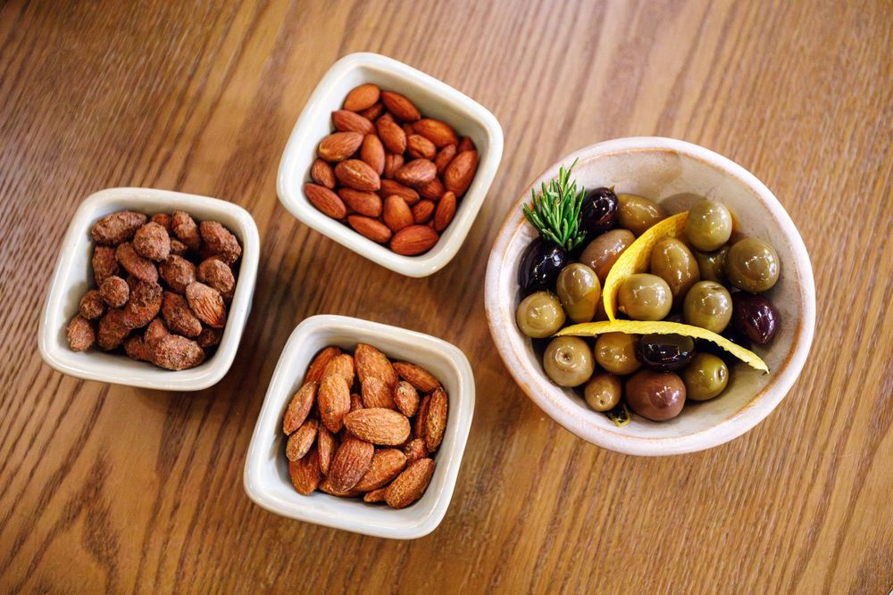 White ceramic bowls filled with almonds and mixed olives on a wooden table surface.