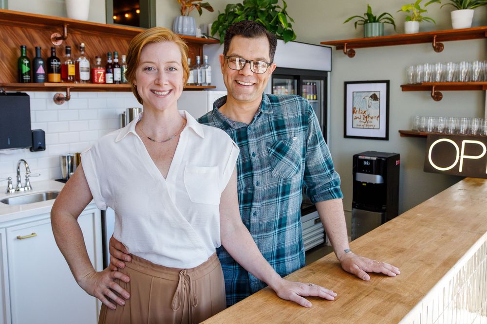 Two restaurant owners stand behind a wooden counter in their casual, modern kitchen space.