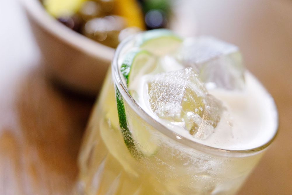 Close up of a refreshing cocktail with lime garnish and ice in a glass against wooden surface.
