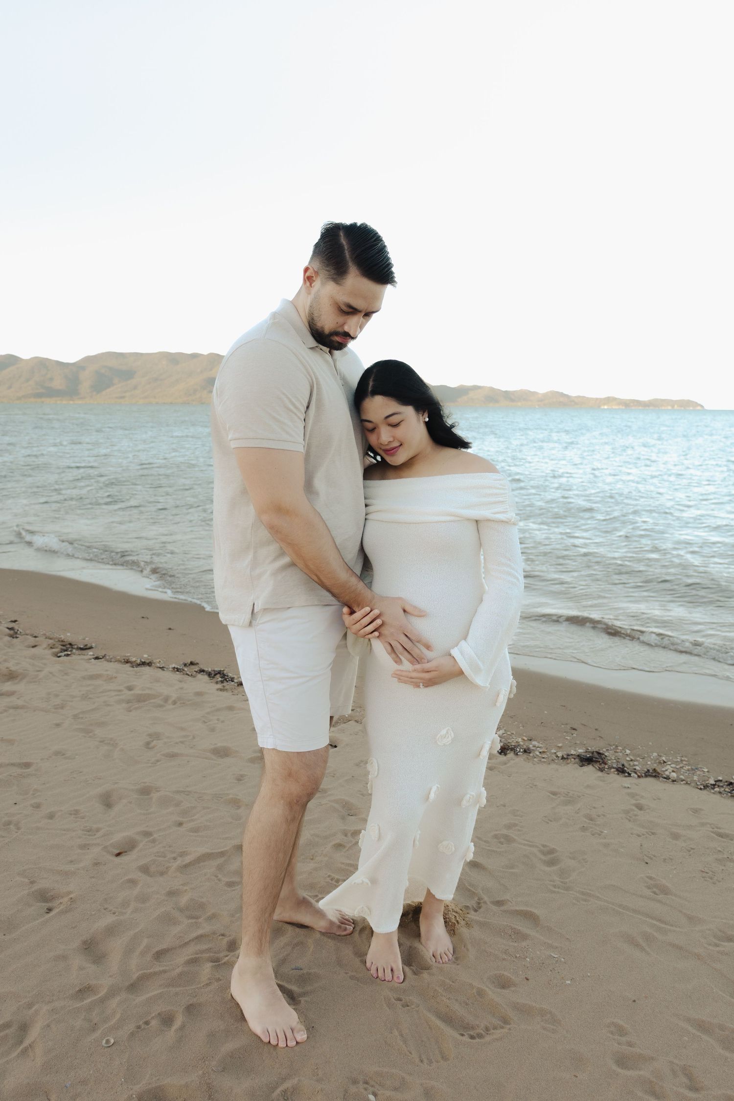 A couple stands together on a beach with gentle waves in the background.