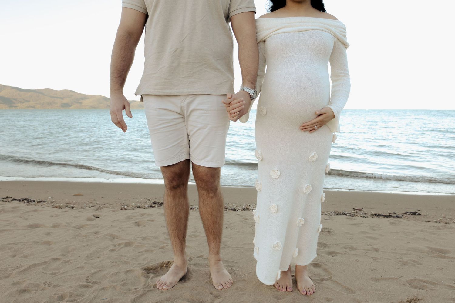 Couple walking barefoot on the beach wearing coordinated white and beige outfits.
