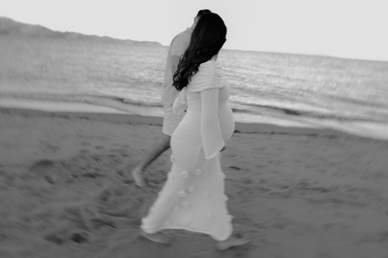 Silhouette of person twirling in white dress on beach with ocean view.