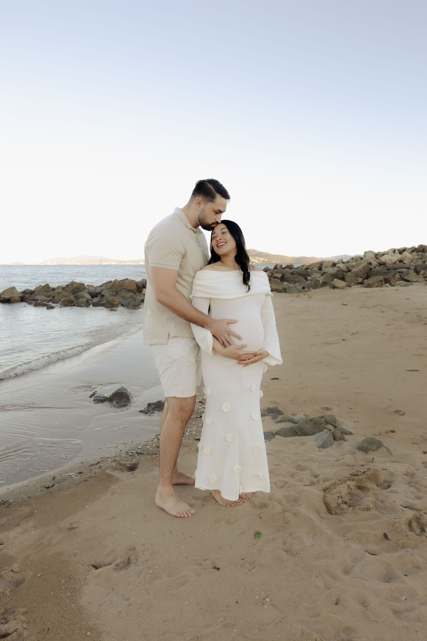 Intimate moment captured on sandy beach with couple in coordinated neutral outfits.
