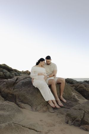 Couple sitting together on coastal rocks during sunset photoshoot.
