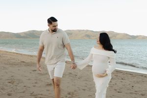 A couple walks hand in hand on a scenic beach with mountains in the background.