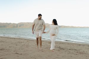 Two people stroll barefoot along a peaceful shoreline at sunset.