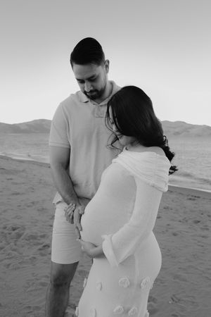 A tender maternity moment captured in black and white on a beach.