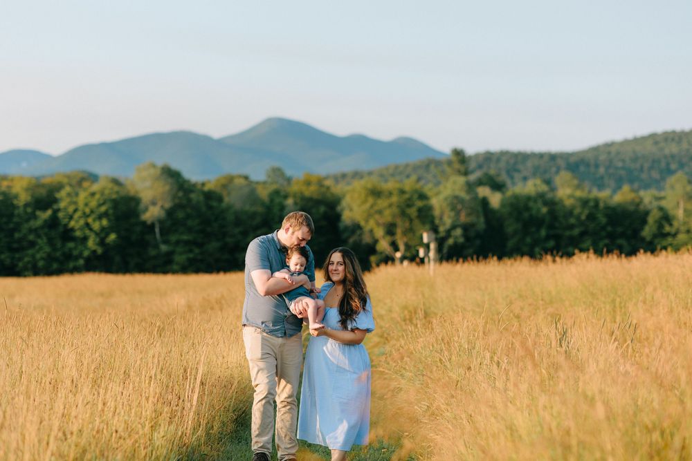 A couple stands together in a golden field with mountains in the distance during sunset.