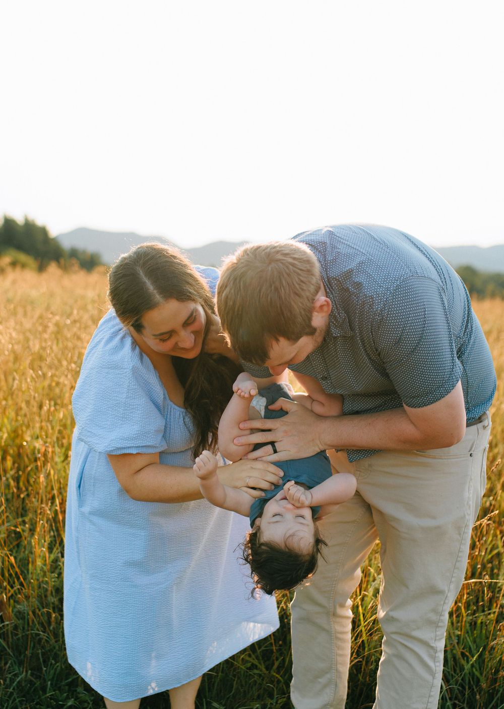 A family plays together in a golden wheat field at sunset, sharing tender moments in the warm evening light.