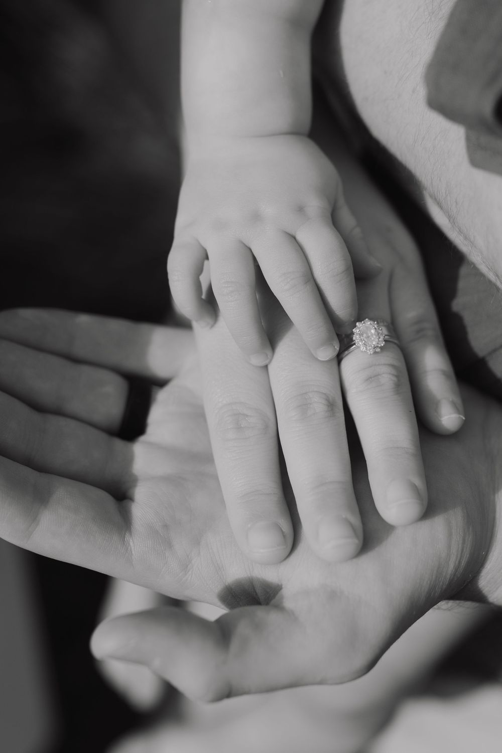 Black and white close-up of a small child's hand resting on an adult's palm, with an engagement ring visible.