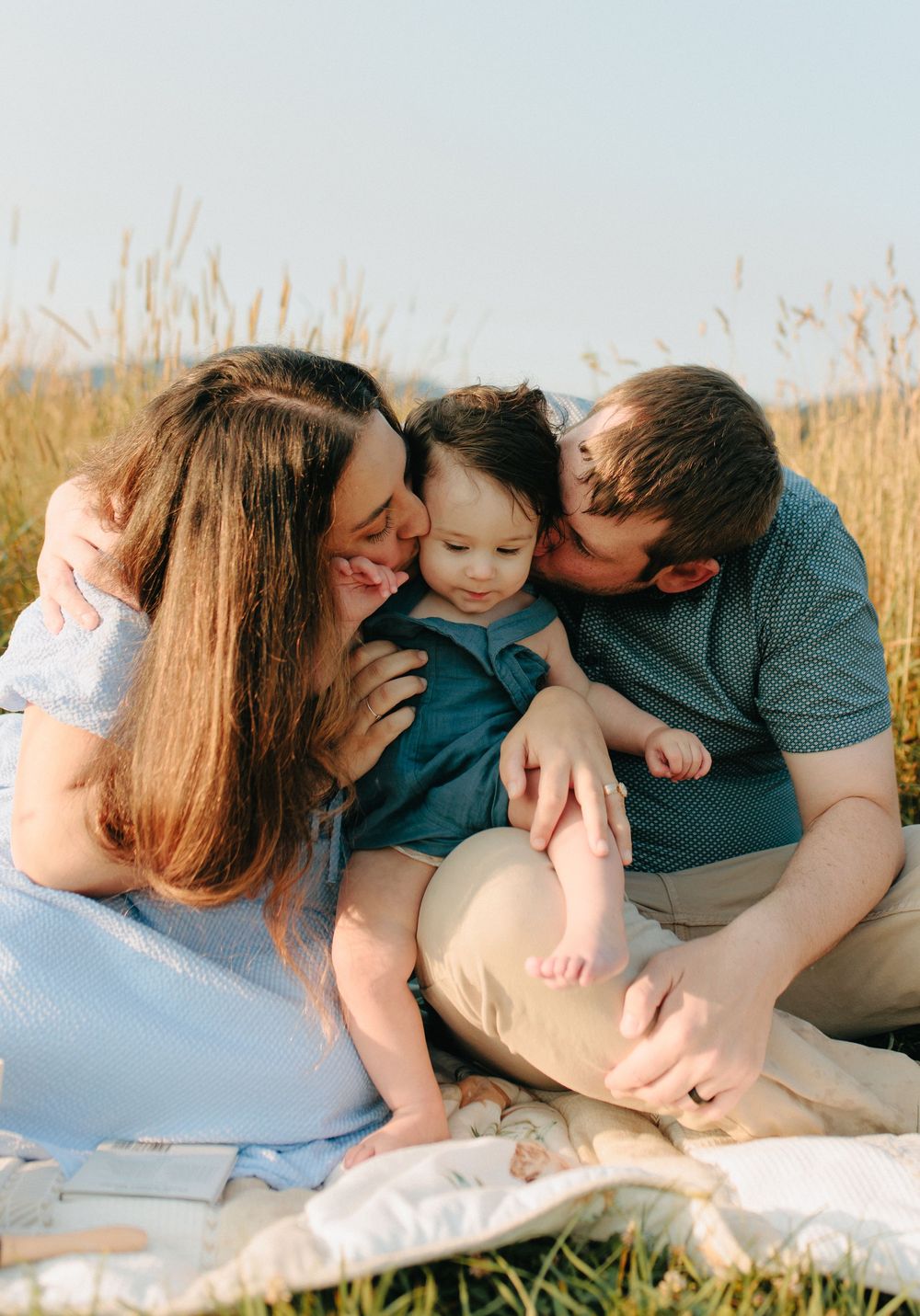 Candid outdoor family photoshoot showing tender moments of affection in golden grassy field at sunset.