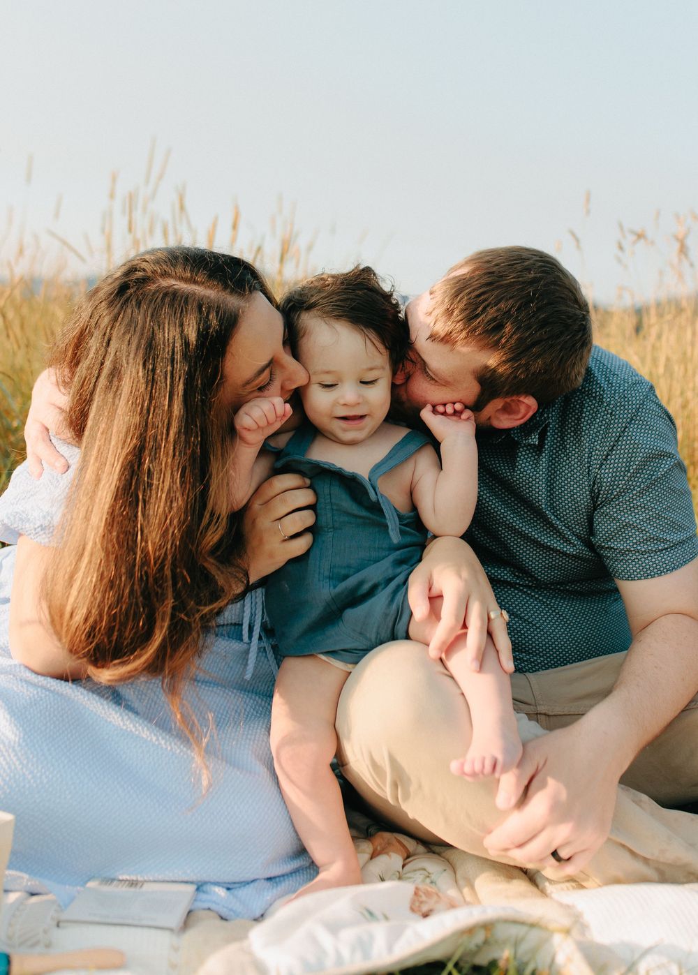 A family shares an intimate moment together while sitting on a blanket in a sunlit field with tall grass.