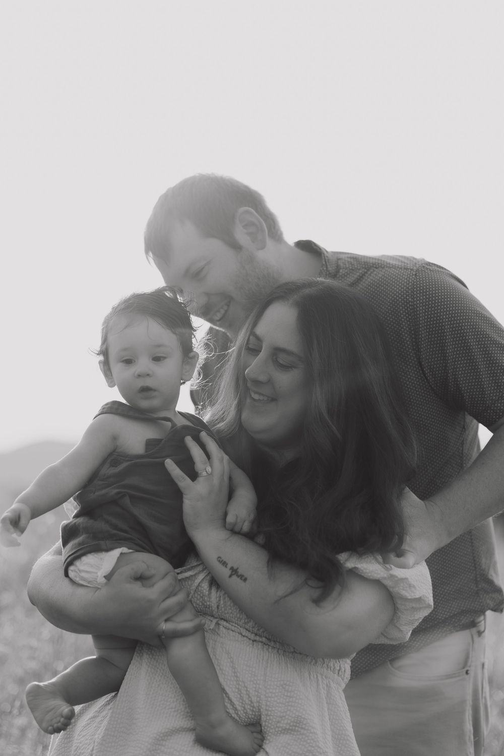 A black and white portrait of a family embracing and smiling together outdoors.