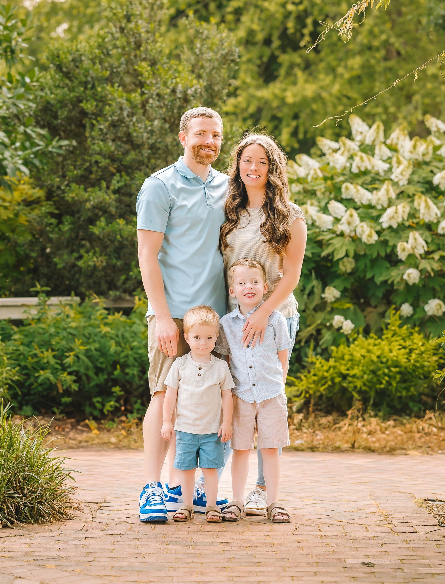 Family laughing and enjoying time together on an outdoor brick patio surrounded by lush greenery on a sunny day.