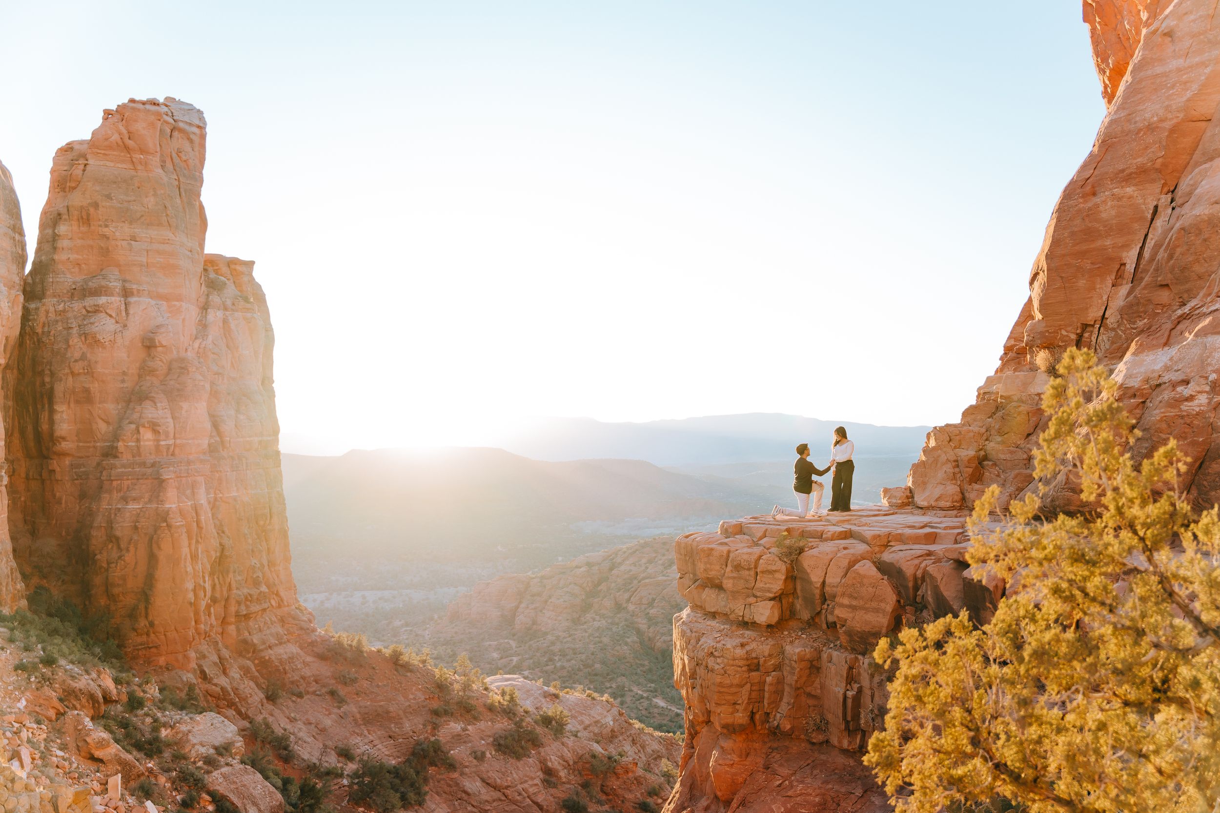 Silhouettes of people on a rocky cliff edge against a mountain landscape.