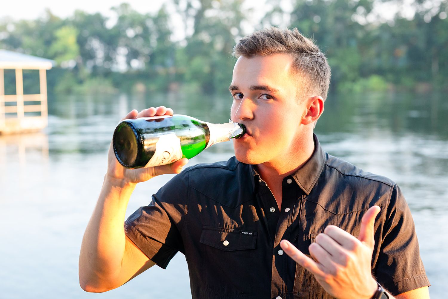 Groom drinks champagne to celebrate engagement by the White River in Cotter, Arkansas.
