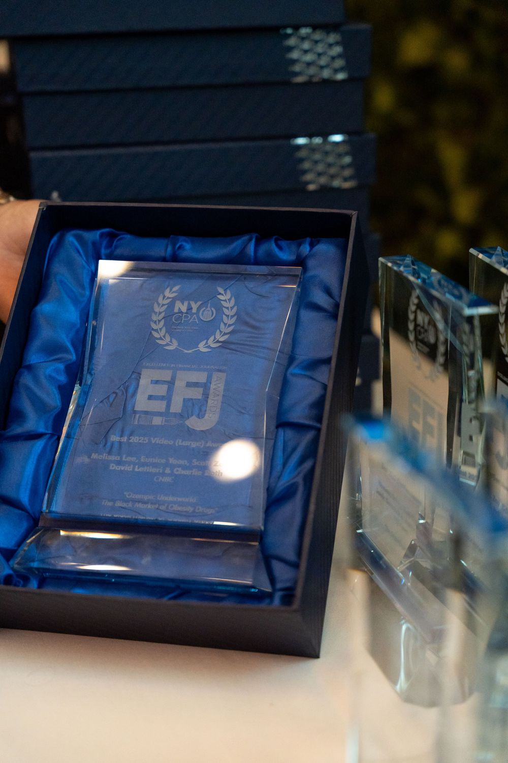 Glass awards displayed in royal blue presentation boxes under lighting.
