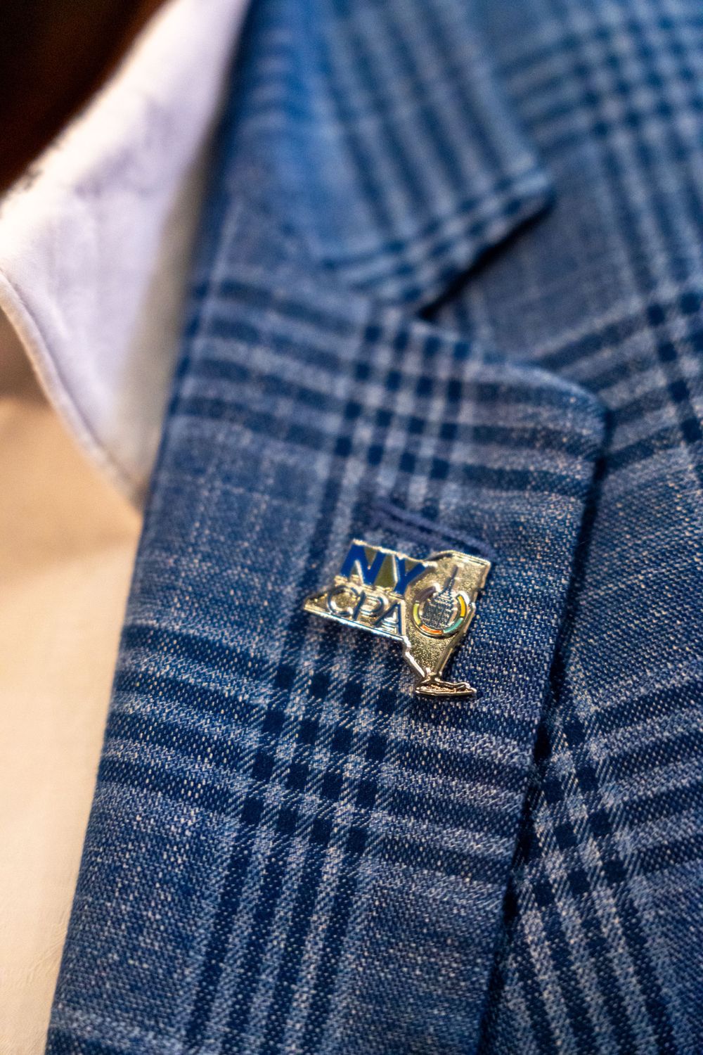 Gold lapel pin details on blue checkered suit fabric.