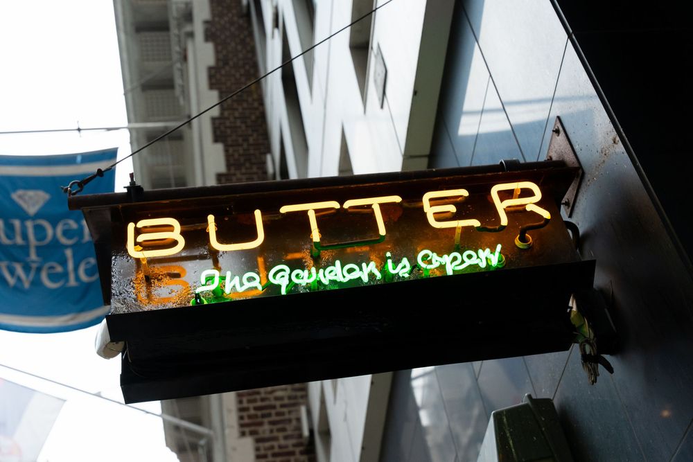 Illuminated business signage for 'BUTTER' against dark urban backdrop.