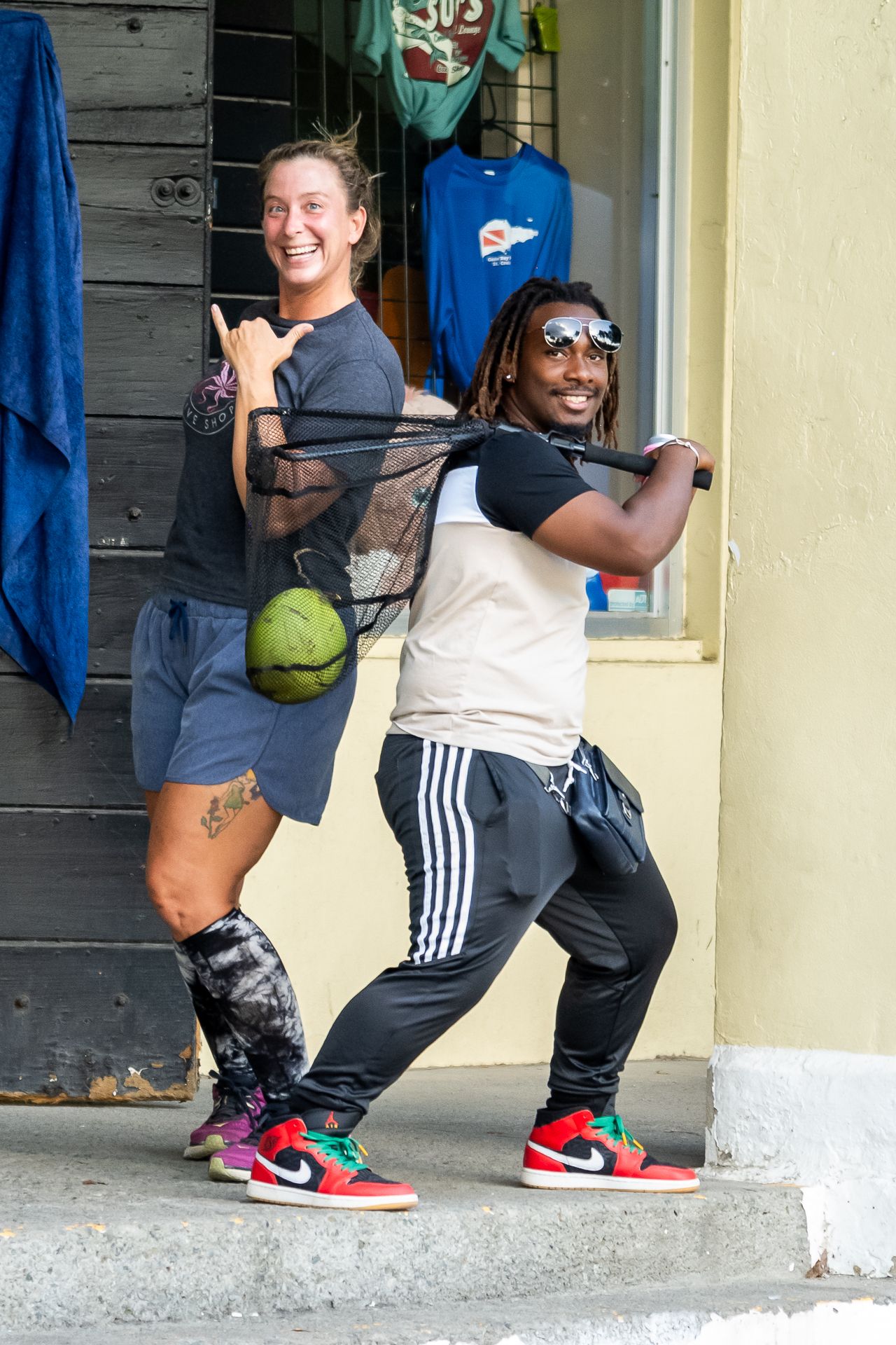 Two friends pose playfully back-to-back on a porch wearing athletic wear and Nike sneakers.