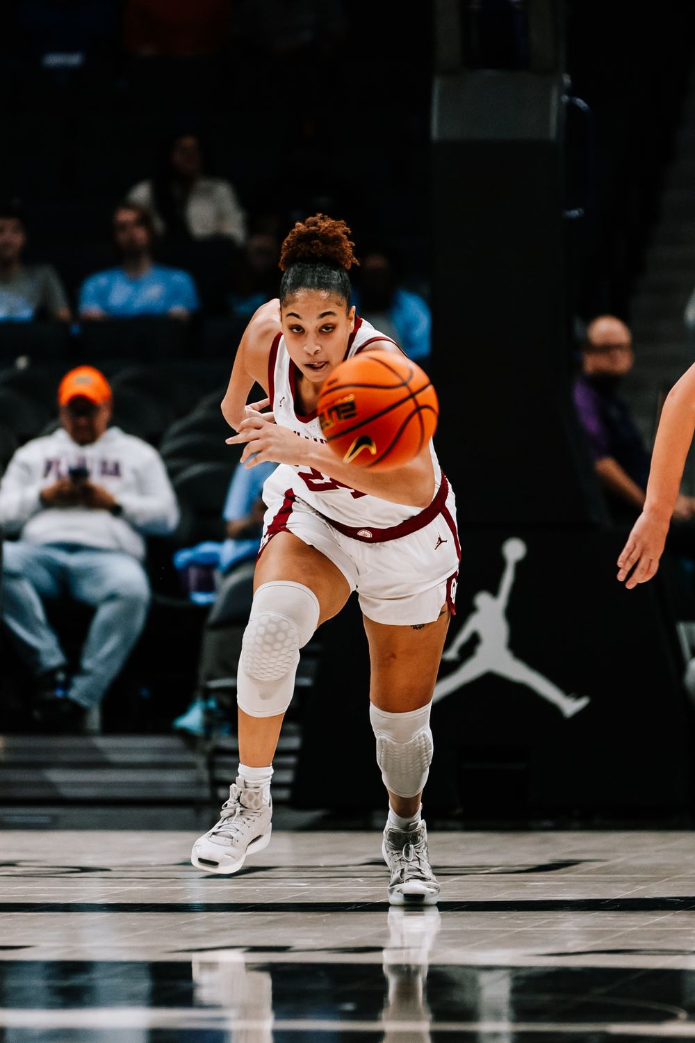 Female basketball player in red uniform drives with ball during women's college basketball game.