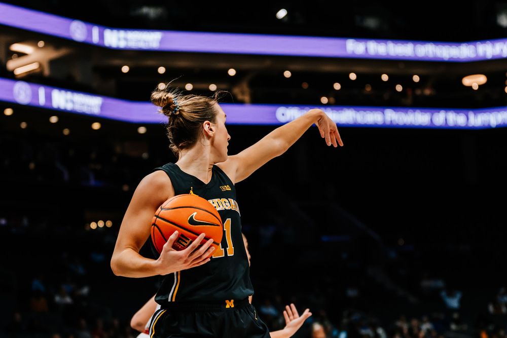 Michigan Wolverines women's basketball player in yellow jersey holds ball during college game.