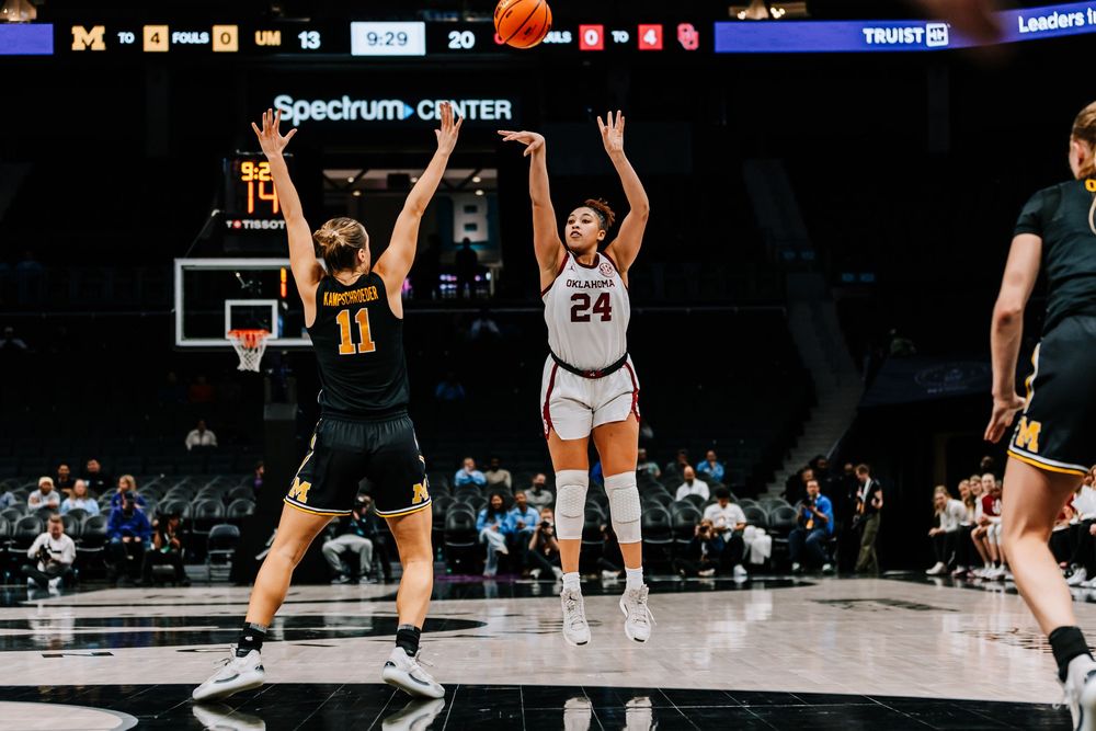 Oklahoma player #24 shoots over Michigan defender #11 during a women's college basketball game.