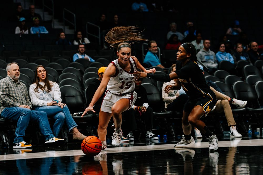A women's college basketball player #15 dribbles past a defender during a game.
