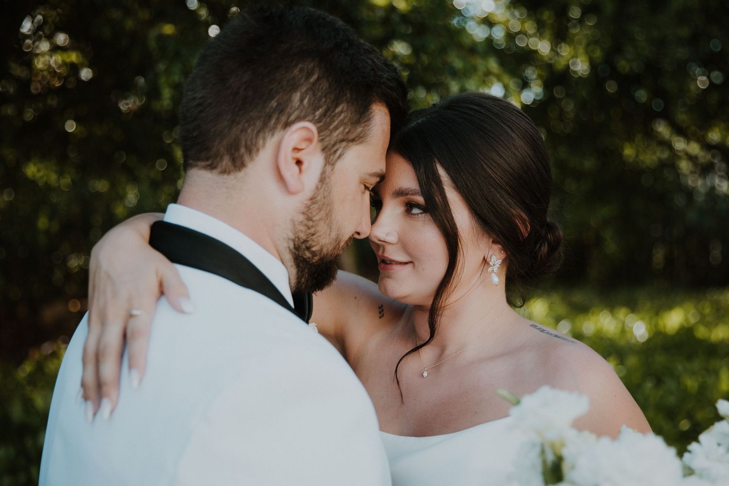 Romantic outdoor wedding portrait of couple embracing in sunlit garden setting.