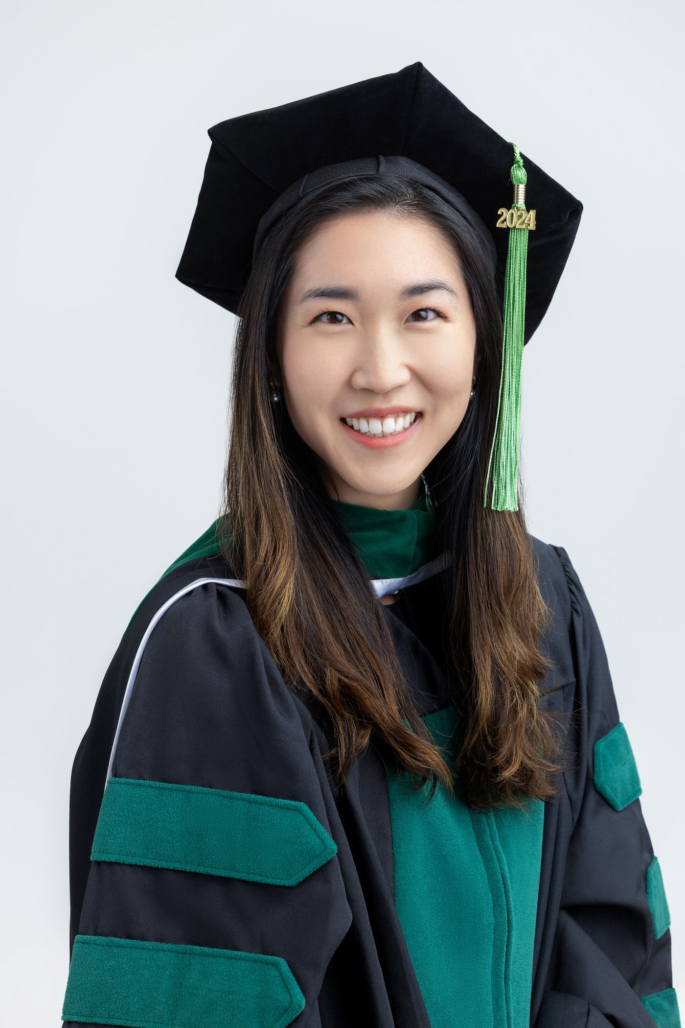Graduate wearing black and green academic regalia with graduation cap and tassel smiles in series of headshot photos.