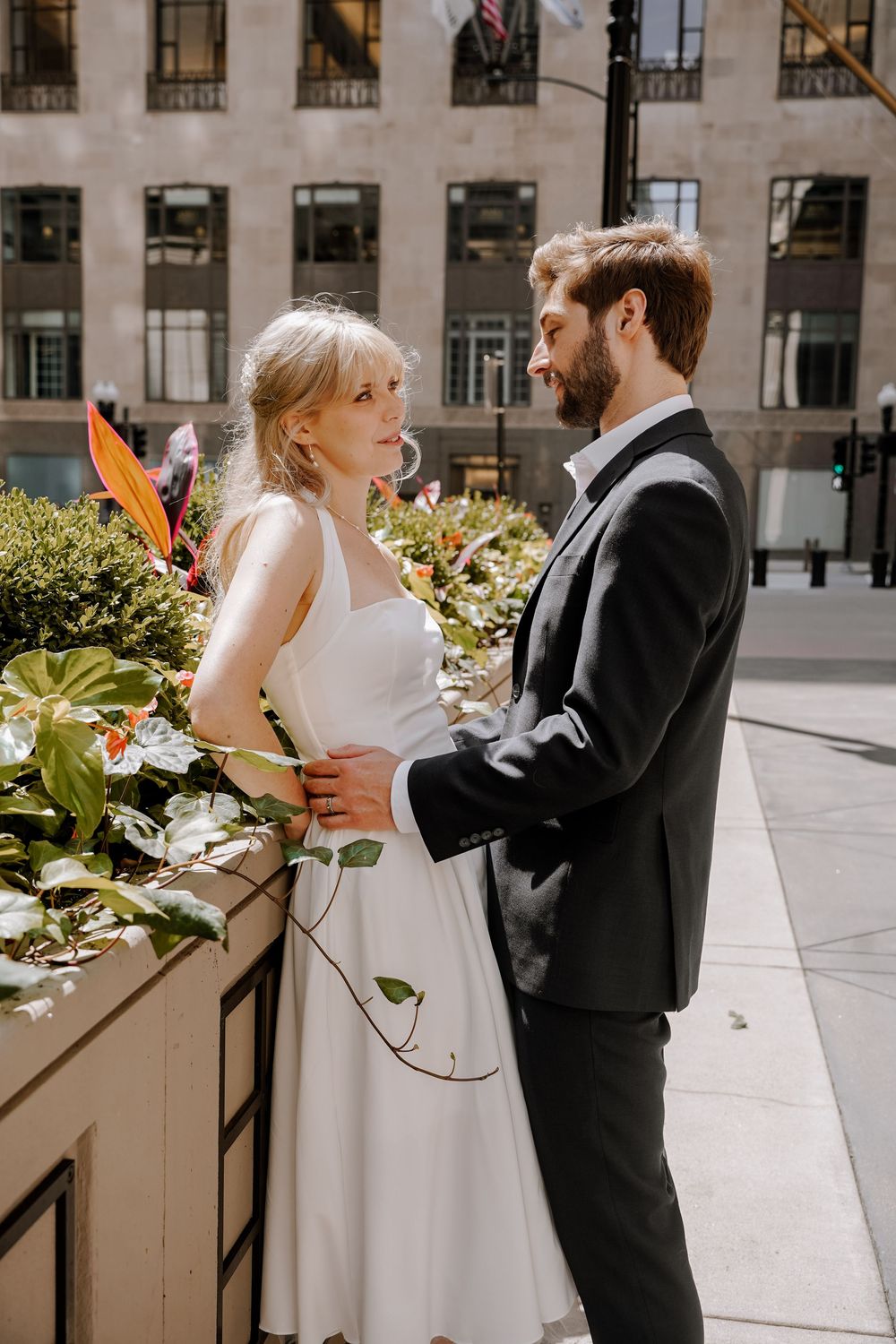 Wedding couple in formal attire sharing a tender moment in a sunlit courtyard with planters.