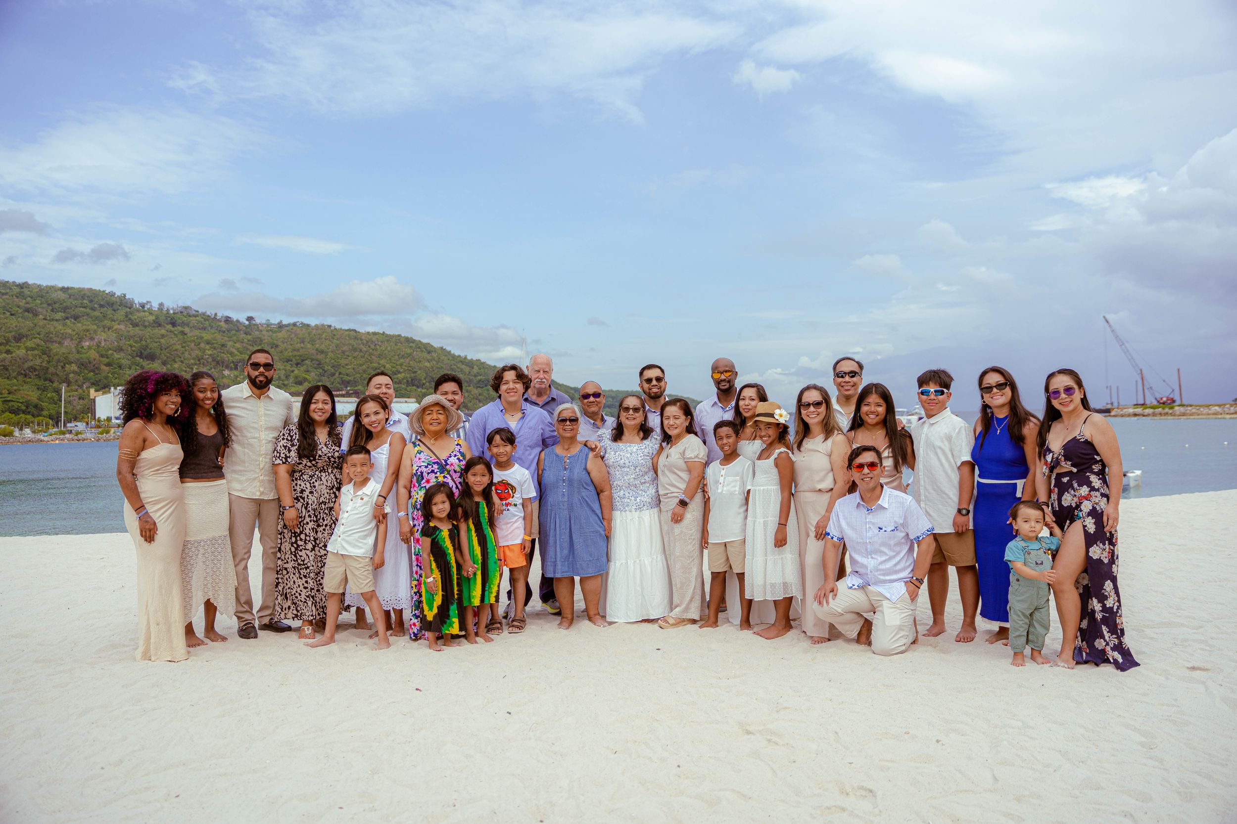 Jamaican Family Photographer Audley Green Large group of beach wedding guests posed together in white and beige attire on a sunny beach.