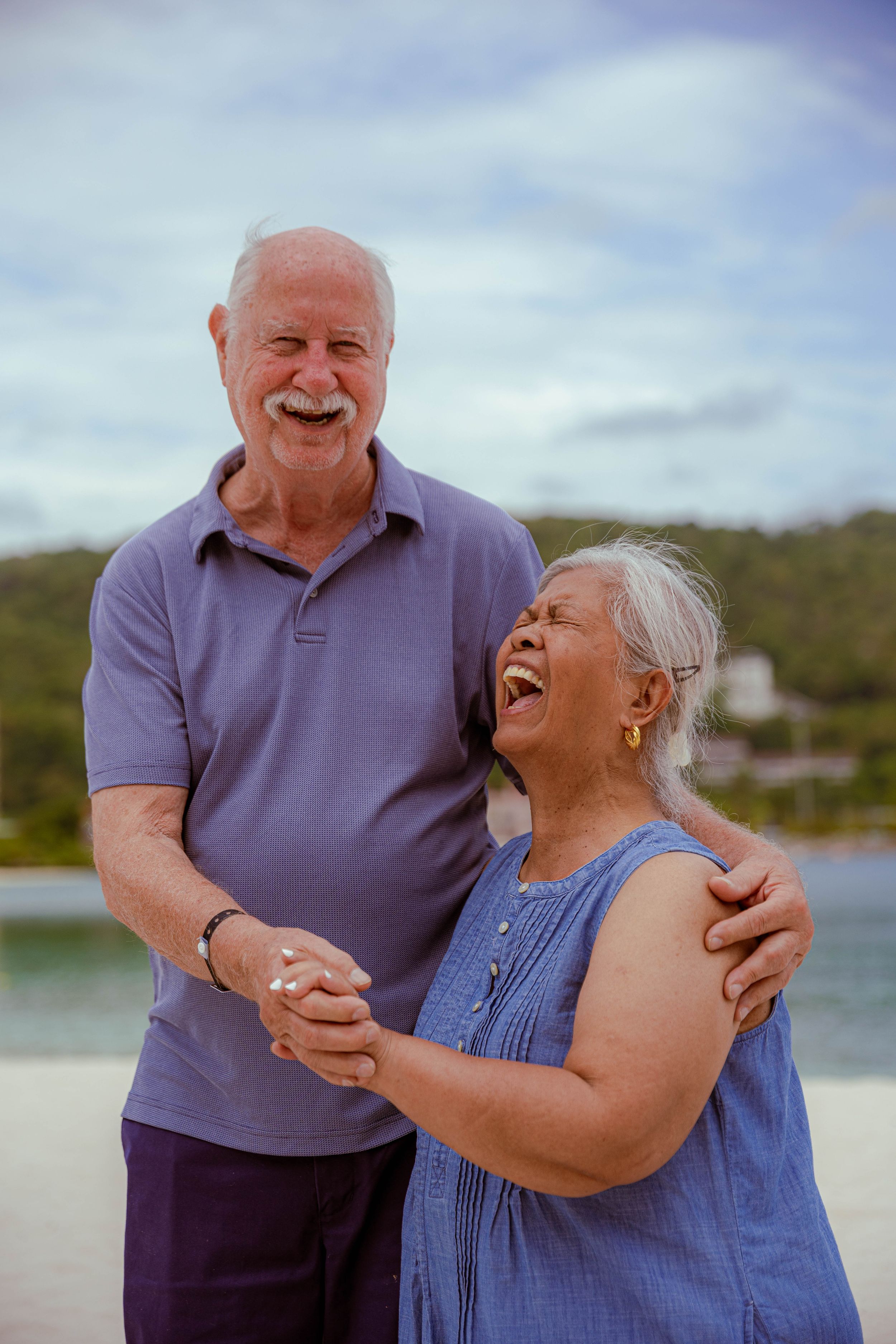 Jamaican Family Photographer Audley Green  Happy senior couple laughing and embracing outdoors near water on a cloudy day.