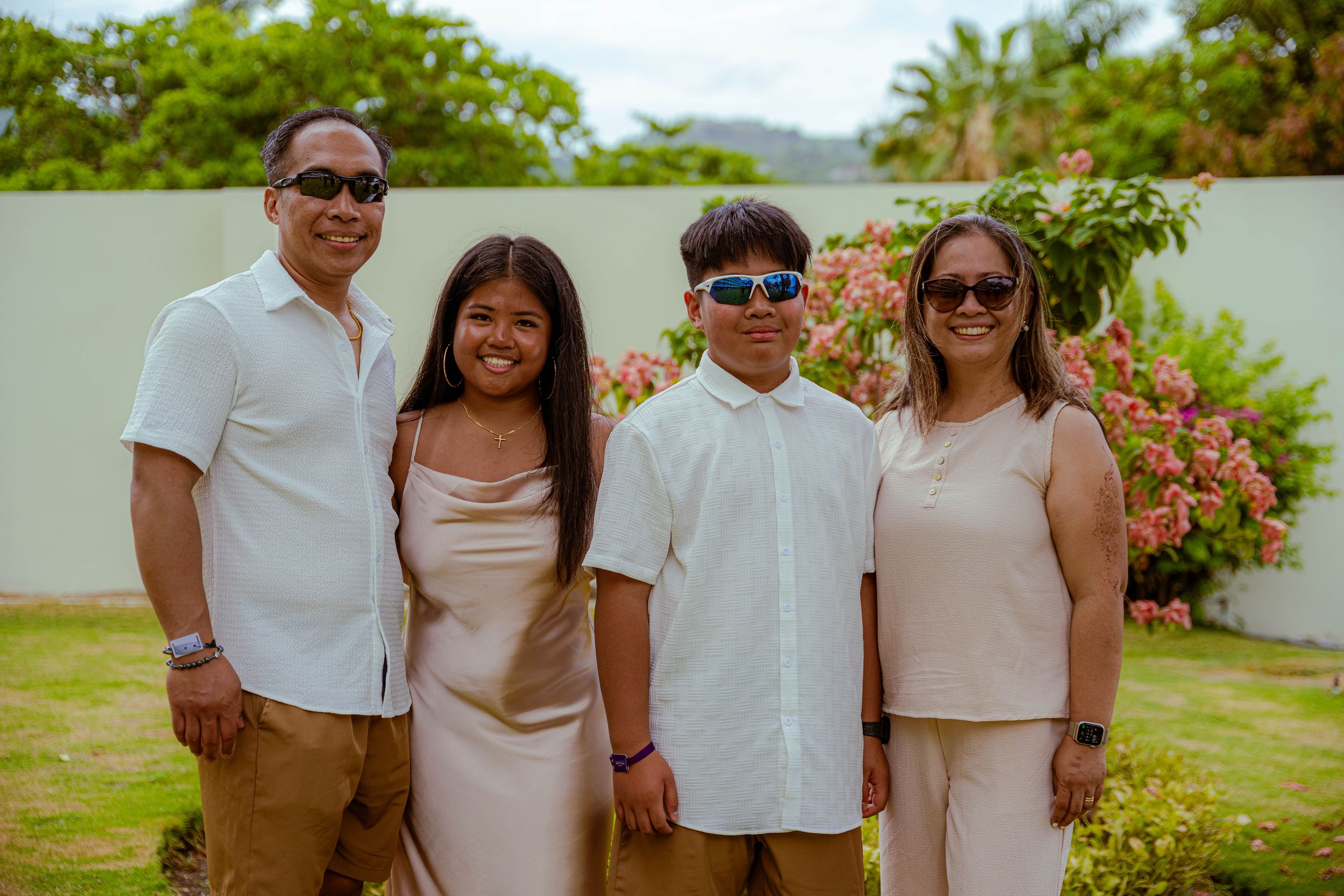 Family in matching light colored outfits posing in garden with tropical flowers and greenery.
