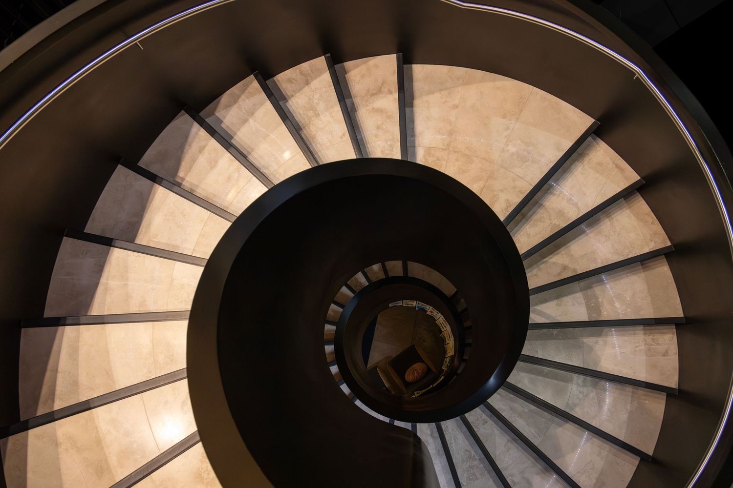 Aerial view of a dramatic spiral staircase with dark railings and stone treads leading into a central void.