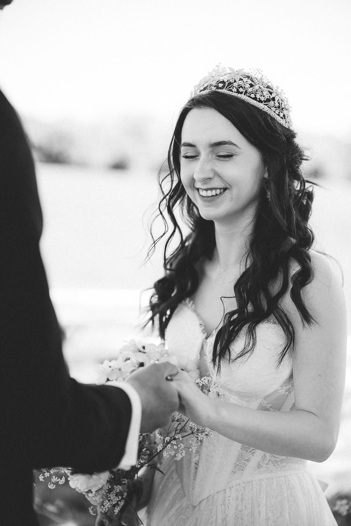 A joyful bride in a sparkling tiara and white gown smiles during an emotional wedding ceremony exchange.